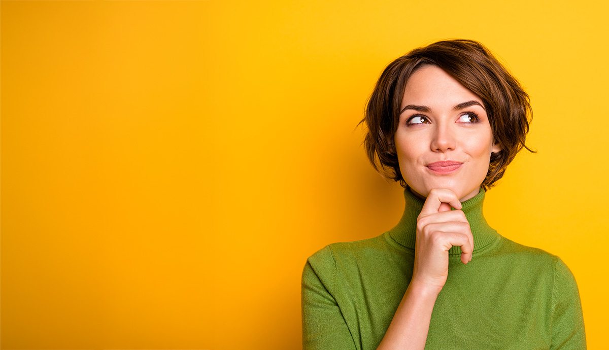 Closeup of short hairdo White woman thinking while looking up with hand on her chin, wearing a green turtleneck and with a yellow background